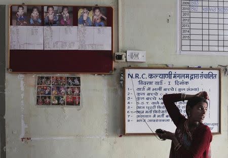 A woman stands next to a board displaying before-and-after treatment pictures of severely malnourished children at the Nutritional Rehabilitation Centre of Shivpuri district in Madhya Pradesh February 1, 2012. REUTERS/Adnan Abidi/Files