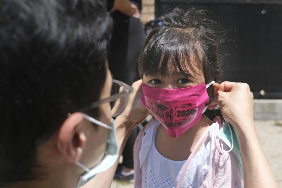 FILE - In this June 10, 2020, file photo, Olivia Chan's father helps her with a new mask she received during a graduation ceremony for her Pre-K class in front of Bradford School in Jersey City, N.J. As the Trump administration pushes full steam ahead to force schools to resume in-person education, public health experts warn that a one-size-fits-all reopening could drive infection and death rates even higher. (AP Photo/Seth Wenig, File)