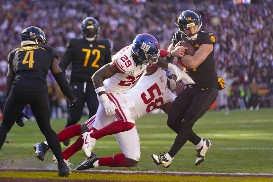 Washington Commanders quarterback Sam Howell (14) is hit by New York Giants safety Xavier McKinney (29) and linebacker Bobby Okereke (58) while scoring a touchdown during the first half of an NFL football game, Sunday, Nov. 19, 2023, in Landover, Md. Also on the field are Washington Commanders wide receiver Curtis Samuel (4) and offensive tackle Charles Leno Jr. (72). (AP Photo/Andrew Harnik)