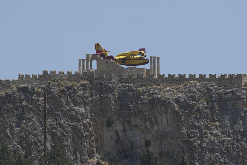 FILE - Canadair aircraft flies behind an archaeological site of Lindos on the Aegean Sea island of Rhodes, southeastern Greece, on July 26, 2023. Tourists at a seaside hotel on the Greek island of Rhodes snatched up pails of pool water and damp towels as flames approached, rushing to help staffers and locals extinguish one of the wildfires threatening Mediterranean locales during recent heat waves. (AP Photo/Petros Giannakouris, File)