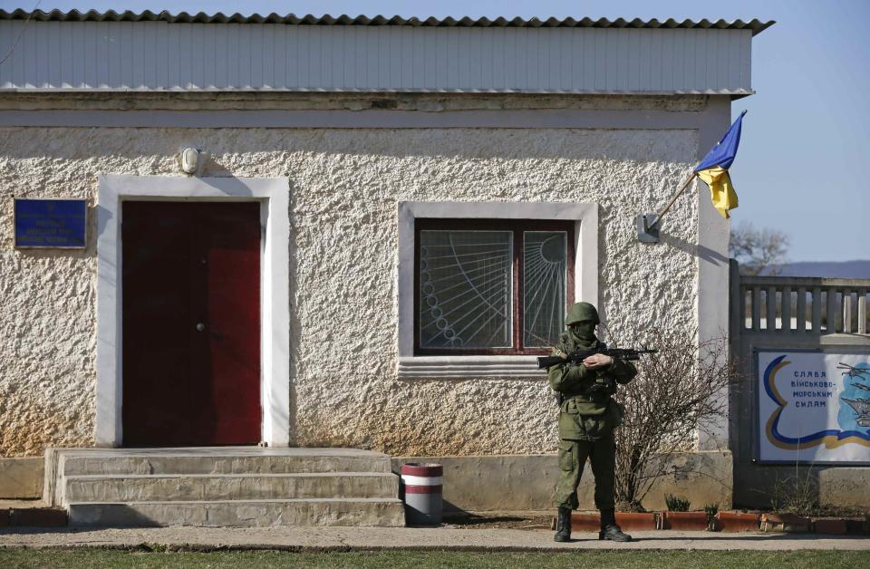 A military personnel member, believed to be a Russian serviceman, stands guard outside the territory of a Ukrainian military unit in the village of Perevalnoye outside Simferopol