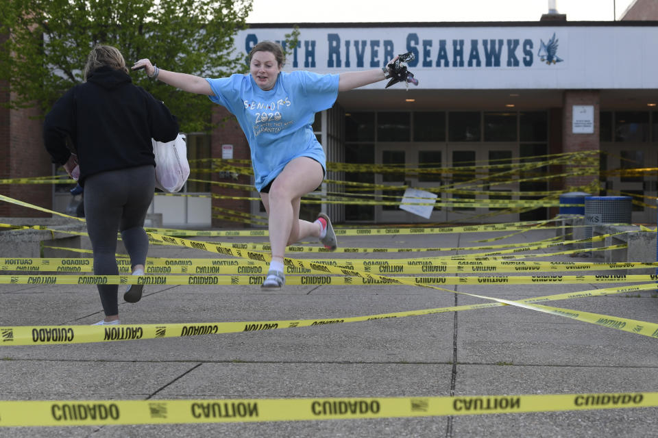 South River High School Class of 2020 senior Aly Yates of Edgewater, Md., jumps over caution tape outside the South River High School in Edgewater, Md., Wednesday, May 13, 2020, as park of a senior prank. Despite the closure of the school because of the coronavirus pandemic, the students are finding ways to keep traditions alive while their family and friends are finding new ways to celebrate and recognize their seniors. (AP Photo/Susan Walsh)