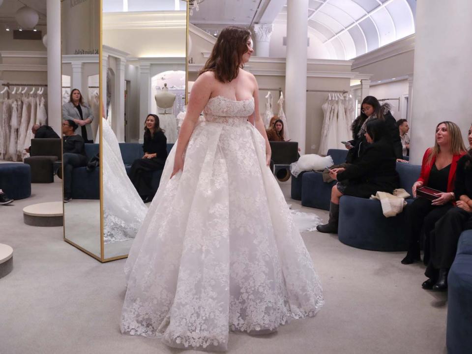 A woman stands in a wedding dress and looks at people sitting on a couch.