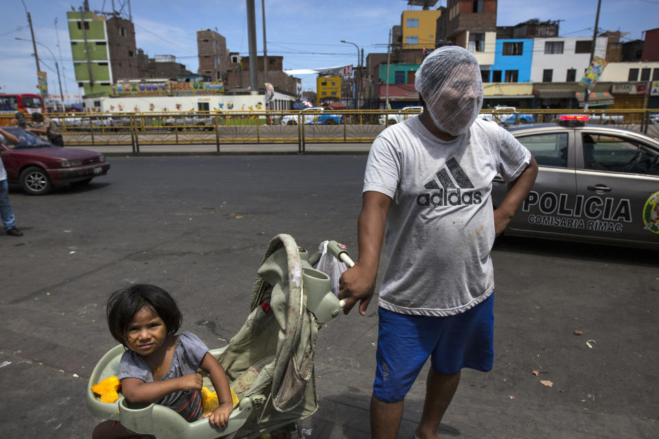 In this March 19, 2020 photo, Luis Mendoza jokingly dons a hair net over his face given to him by a group handing out protective gear outside a popular market where he has come to beg for food with his 2-year-old daughter Alejandra, in Lima, Peru. The global COVID-19 pandemic has spotlighted the wide gap between the rich and poor in Latin America and economists say a looming economic recession worse than any since World War II could push the continent's long-suffering poor into even more dire circumstances. (AP Photo/Rodrigo Abd)