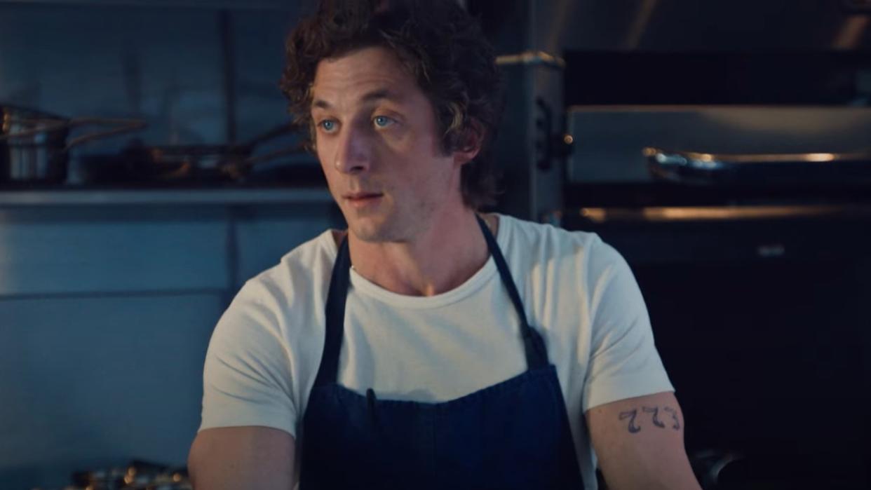  Jeremy Allen White as Carmy in The Bear wearing an apron and standing in a kitchen. 
