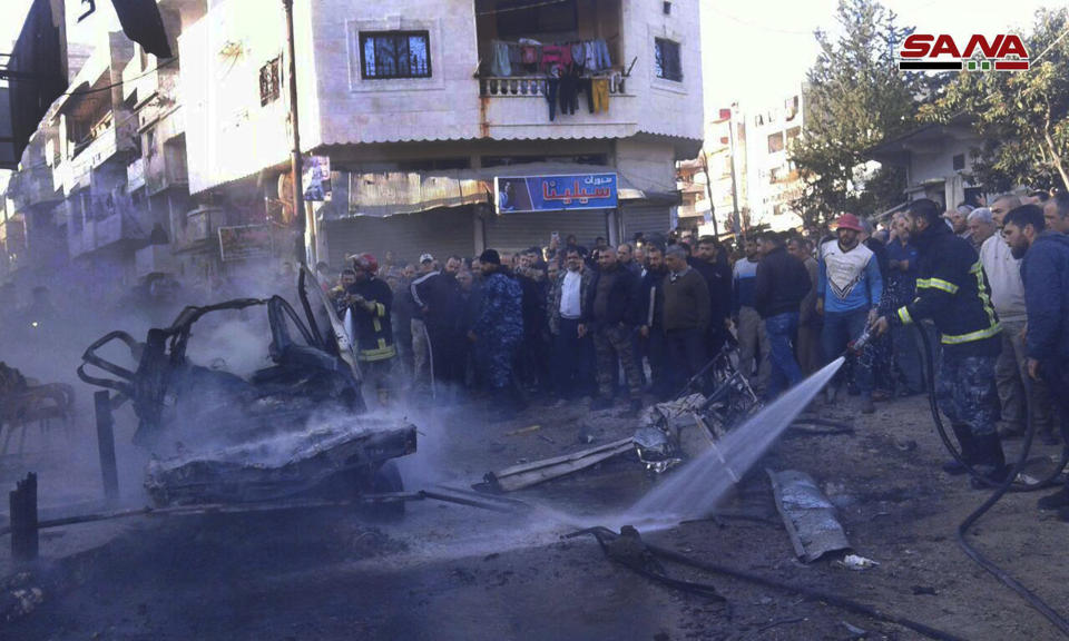 In this photo released by the Syrian official news agency SANA, a Syrian firefighter extinguishes a burned car at the site of a deadly explosion, in the coastal city of Latakia, Syria, Tuesday, Jan. 22, 2019. Syrian state TV said Tuesday's blast was a car bomb that went off in Al-Hammam Square in Latakia that has been a government stronghold since the conflict began in March 2011. (SANA via AP)