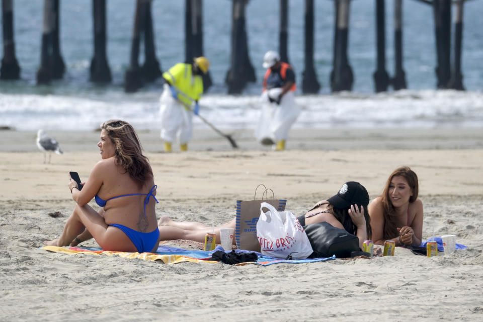 Beach goers are seen as workers in protective suits clean the contaminated beach after an oil spill, Wednesday, Oct. 6, 2021 in Newport Beach, Calif. A major oil spill off the coast of Southern California fouled popular beaches and killed wildlife while crews scrambled Sunday, to contain the crude before it spread further into protected wetlands. (AP Photo/Ringo H.W. Chiu)