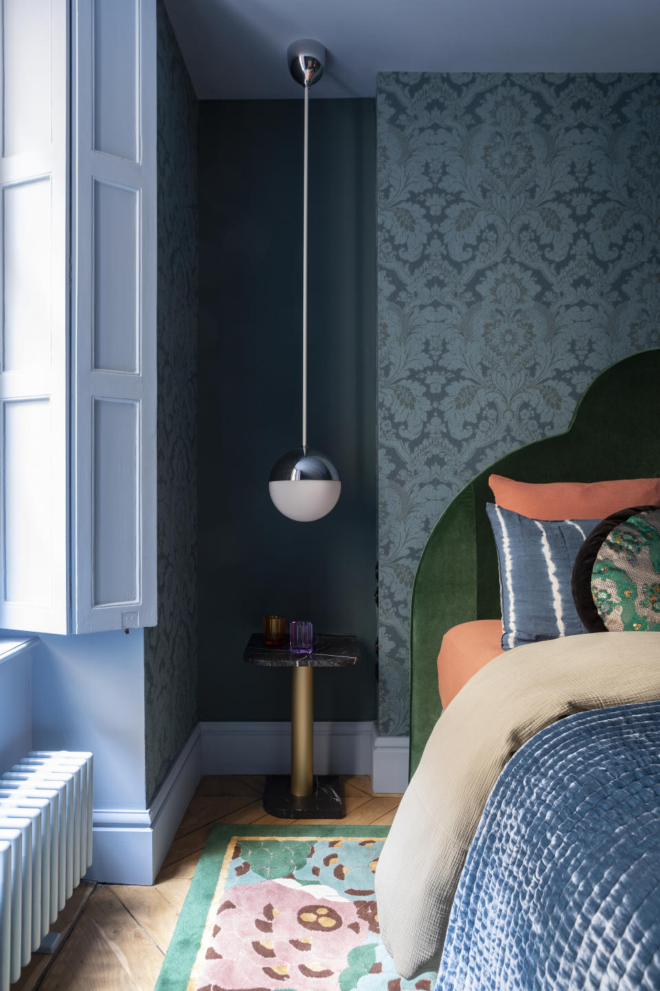 A bedroom with light blue windows and dark blue bedding, along with green headboard