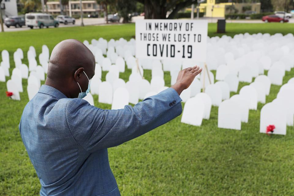 Vice Mayor Alix Desulme of North Miami, Florida, raises his arm during a prayer for local lives lost to COVID-19 as a memorial to those lost is unveiled at Griffing Park on October 28, 2020. Five hundred plastic cardboard tombstones were placed in the ground honoring COVID-19 victims.