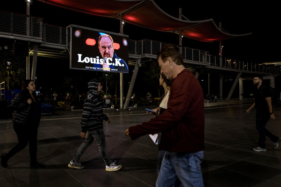 In this Thursday, Nov. 28, 2019 photo, Israelis walk past a billboard showing Comedian Louis C.K. in the Israeli city of Holon near Tel Aviv. Two years after being swept up in the Me Too movement and acknowledging sexual misconduct with multiple women, comedian Louis C.K. took to the stage at a nearly packed basketball arena outside Tel Aviv, where the audience seemed ready to let it go.(AP Photo/Tsafrir Abayov)