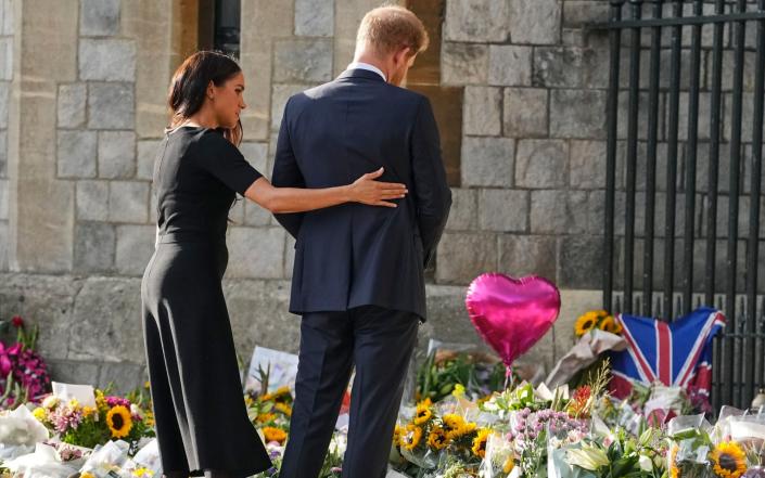 شاهزاده هری و مگان، دوشس ساسکس، به ادای احترام به گل ملکه فقید الیزابت دوم در خارج از قلعه ویندزور نگاه می کنند - مارتین مایسنر/AP
