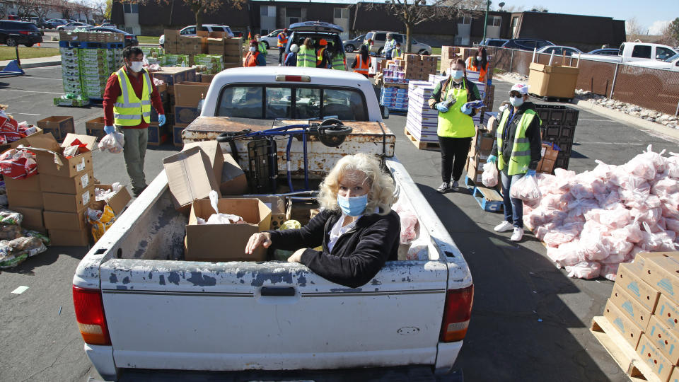 A woman rides in the back of a pick-up truck as cars line up for food at the Utah Food Bank's mobile food pantry Monday, April 20, 2020, in Orem, Utah. As coronavirus concerns continue, the need for assistance has increased, particularly at the Utah Food Bank. (AP Photo/Rick Bowmer)