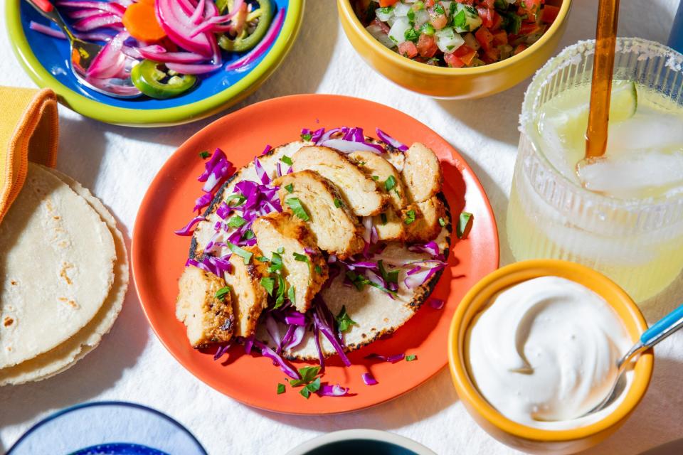 A platter of cooked, sliced cultivated chicken sprinkled with red cabbage, with a side of sour cream.