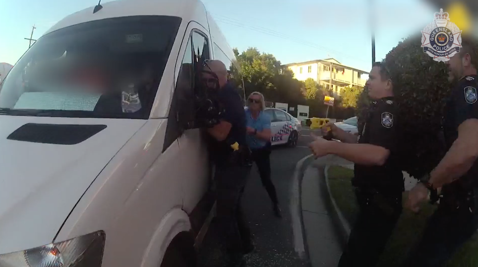 A police officer holds a Taser while another reaches into the Blue Care bus after pulling it over in Maroochydore.