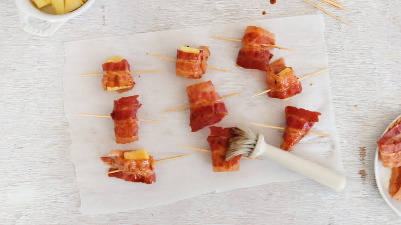 brushing bacon-wrapped pineapple with sauce