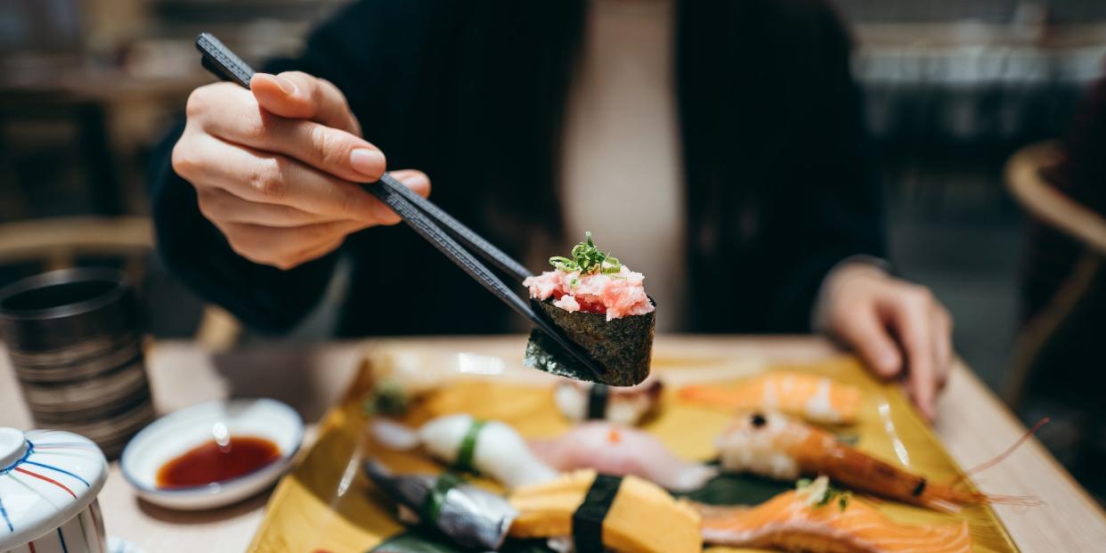 Young Asian woman eating freshly made sushi with side dish and green tea in a Japanese restaurant.