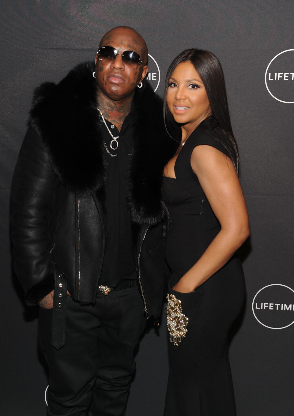 Two people posing together, one in a fur-trimmed jacket, the other in a fitted dress, at a Lifetime event