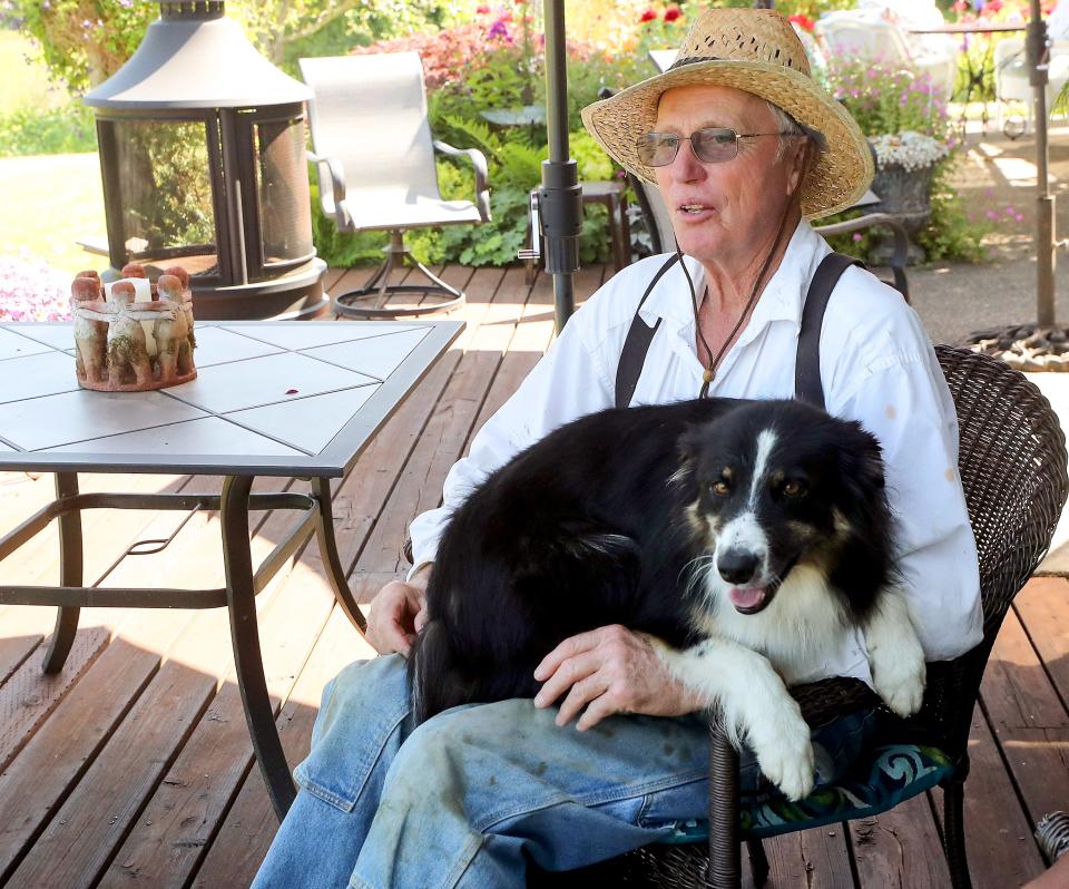 Jay Allen looks down at the haying taking place in the field below his home as his dog Rosie sits in his lap on July 13.