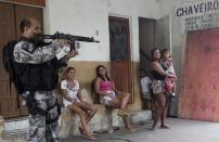 Residents observe a police officer take up position during an operation at the Mare slums complex in Rio de Janeiro March 25, 2014. Brazil will deploy federal troops to Rio de Janeiro to help quell a surge in violent crime following attacks by drug traffickers on police posts in three slums on the north side of the city, government officials said on Friday. Less than three months before Rio welcomes tens of thousands of foreign soccer fans for the World Cup, the attacks cast new doubts on government efforts to expel gangs from slums using a strong police presence. The city will host the Olympics in 2016. REUTERS/Ricardo Moraes (BRAZIL - Tags: CRIME LAW)