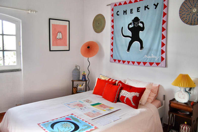 Cheeky monkey art tapestry hung above bed in white bedroom.