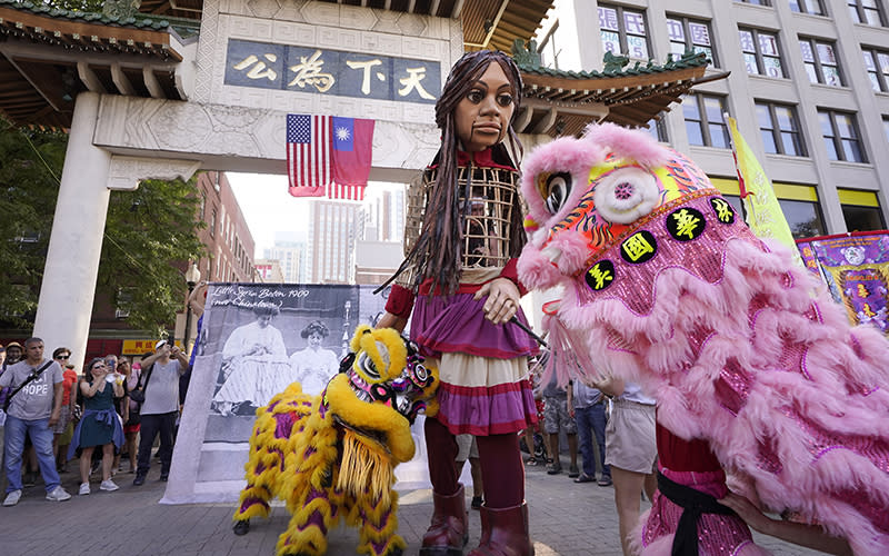 Little Amal, a 12-foot puppet of a 10-year-old Syrian refugee girl, center, is greeted by performers in lion dance costumes