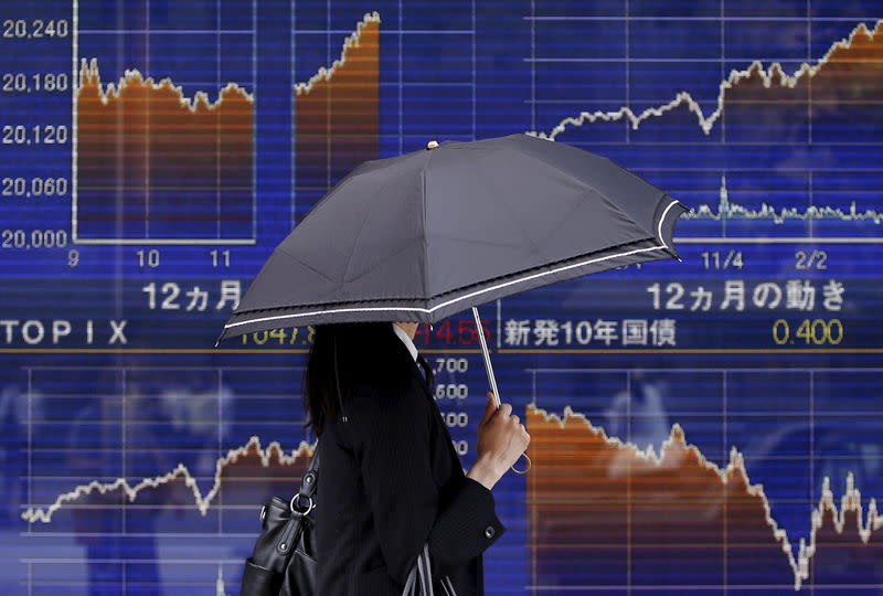 A pedestrian holding an umbrella walks past an electronic board showing the graph of the recent fluctuations of Japan's Nikkei average outside a brokerage in Tokyo, Japan, May 20, 2015. REUTERS/Yuya Shino