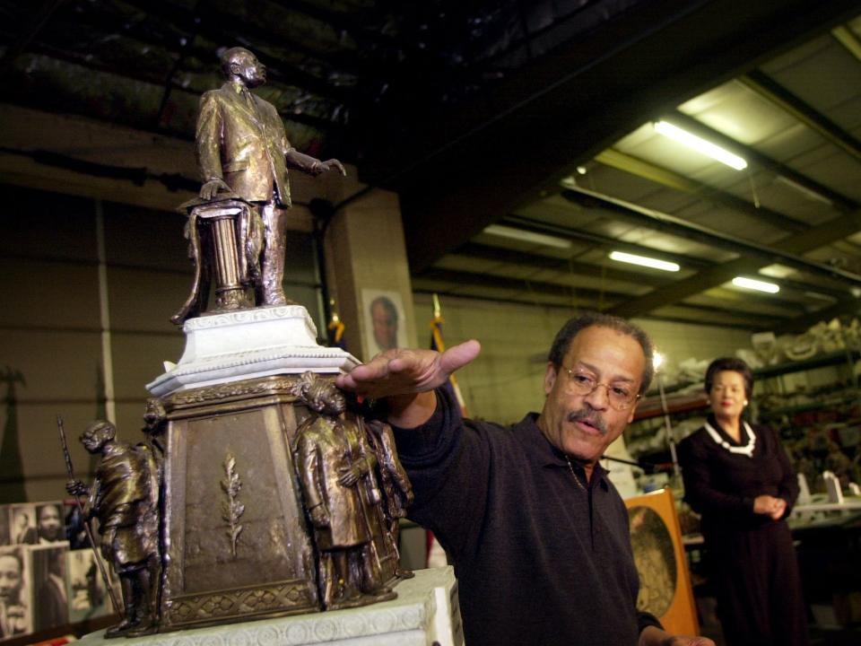 Ed Dwight motions to a bronze statue he sculpted while a woman looks on in the distance