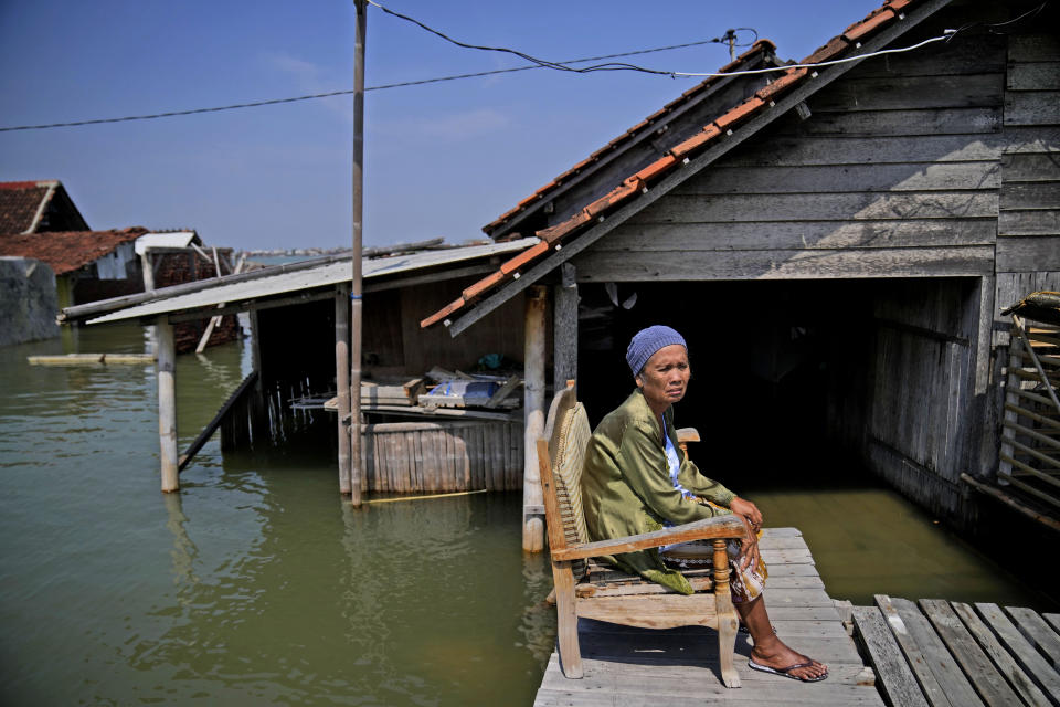 Mar'iah sits outside her house while waiting for the flood water to subside in Timbulsloko, Central Java, Indonesia, Sunday, July 31, 2022. Mar'iah explains that she sits in the chair every day waiting until her house is dry enough to enter again. (AP Photo/Dita Alangkara)