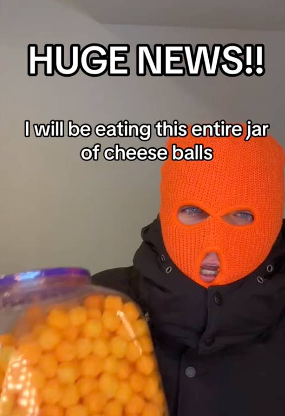 Person in black attire and orange mask holding a jar of cheese balls, text "HUGE NEWS!! I will be eating this entire jar of cheese balls" above