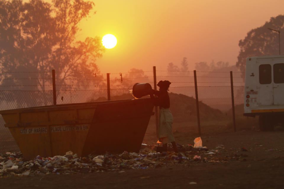 A woman throws away garbage at a dumpsite in Harare, Friday, Aug, 9, 2019. Fuel prices and the cost of living continue to rise in Zimbabwe due to the volatility of the recently introduced new currency, as the population struggles with water and power shortages. (AP Photo/Tsvangirayi Mukwazhi)