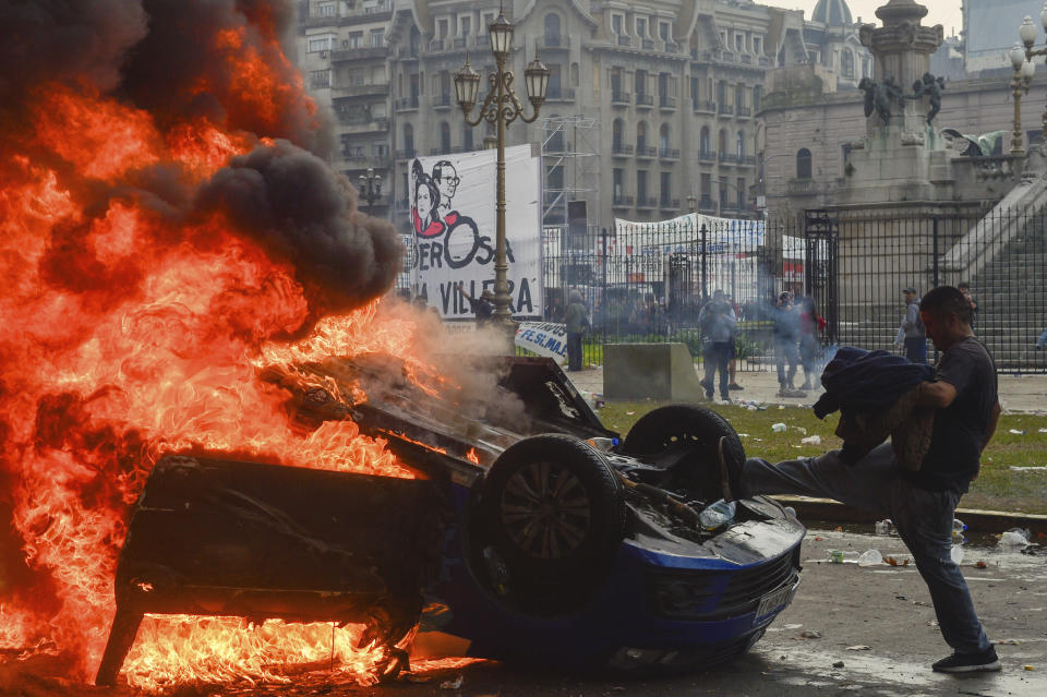 An anti-government protester kicks a burning vehicle during clashes with police outside Congress, where lawmakers debate a reform bill promoted by Argentine President Javier Milei in Buenos Aires, Argentina, Wednesday, June 12, 2024. (AP Photo/Gustavo Garello)