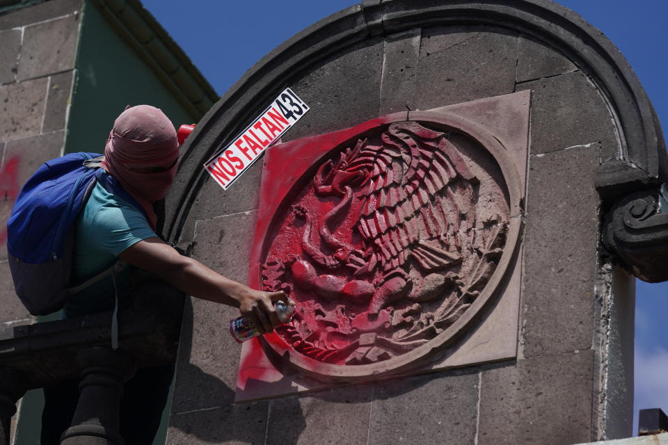 A demonstrator uses red spray paint to symbolize blood over a national symbol outside a military base in Mexico City, Friday, Sept. 23, 2022, days before the anniversary of the 2014 disappearance of 43 college students in Iguala, Guerrero. The sign reads in Spanish "We're missing 43!" One week prior, Mexican authorities said they arrested a retired general and three other members of the army for alleged connection to their disappearance. (AP Photo/Fernando Llano)