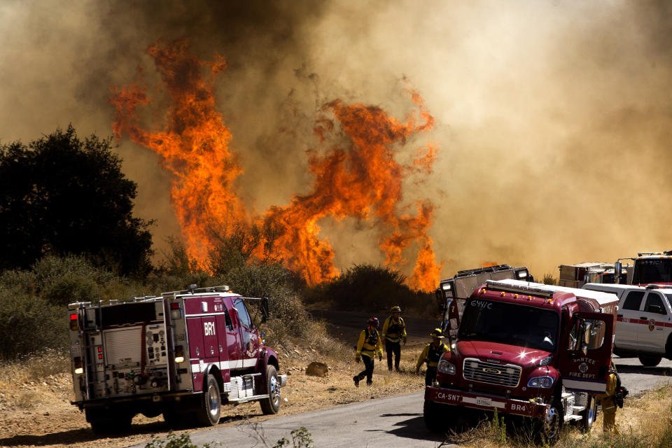 Flames from flare behind firefighters and fire trucks at the Apple Fire in Cherry Valley, Calif., Saturday, Aug. 1, 2020. A wildfire northwest of Palm Springs flared up Saturday afternoon, prompting authorities to issue new evacuation orders as firefighters fought the blaze in triple-degree heat. (AP Photo/Ringo H.W. Chiu)