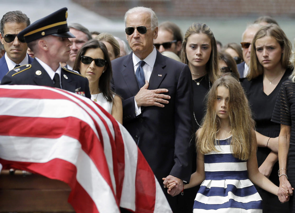 Joe Biden, accompanied by his family, holds his hand over his heart as he watches an honor guard carry a casket containing the remains of his son Beau Biden.