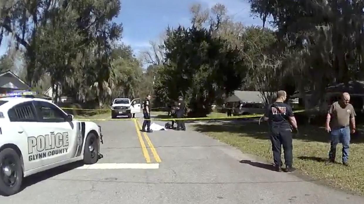 In this Feb. 23, 2020 image taken from Glynn, Ga., County Police body camera video, authorities, rear, stand over the covered body of Ahmaud Arbery, who was shot and killed while while running in a neighborhood outside the port city of Brunswick, Ga.