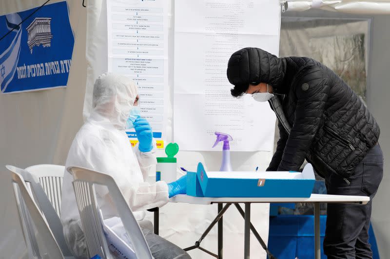 A paramedic in a protective suit helps a man as he prepares to vote in a special polling station set up by Israel's election committee so Israelis under home-quarantine can vote in Israel's national election, in Ashkelon, Israel