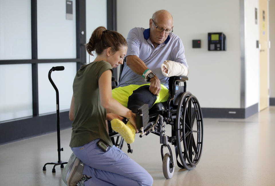 William Lytton, of Scarsdale, N.Y., right, is assisted by physical therapist Caitlin Geary, left, at Spaulding Rehabilitation Hospital, in Boston, Tuesday, Aug. 28, 2018, while recovering from a shark attack. Lytton suffered deep puncture wounds to his leg and torso after being attacked by a shark on Aug. 15, 2018 while swimming off a beach, in Truro, Mass. Lytton injured a tendon in his arm while fighting off the shark. (AP Photo/Steven Senne)