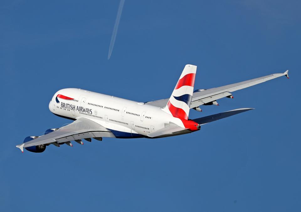 A British Airways Airbus A380 flies across a blue sky with the trail of a smaller plane visible in the far distance