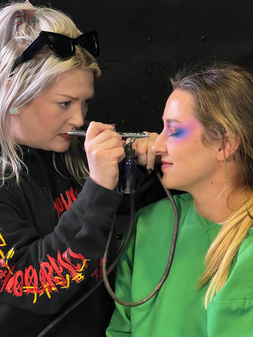 A makeup artist airbrushes a performer before the night's Mardi Gras parade. Hundreds of team members work behind the scenes to produce the months-long event.