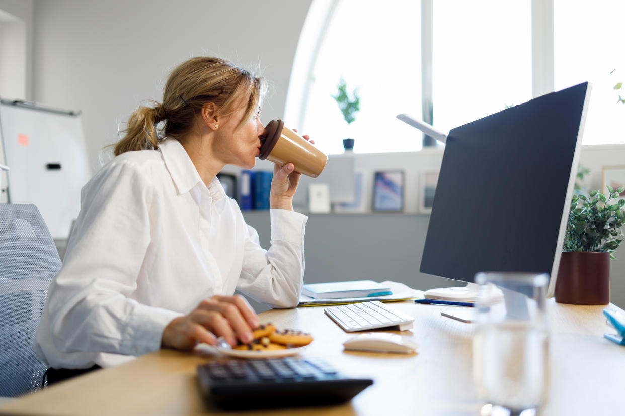 Focused on working at the computer business woman drinking coffee with cookies in the office