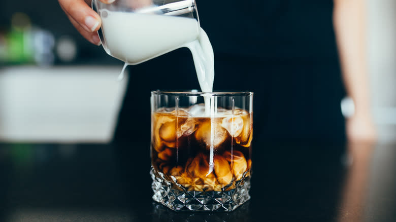 pouring milk into glass of cold brew coffee