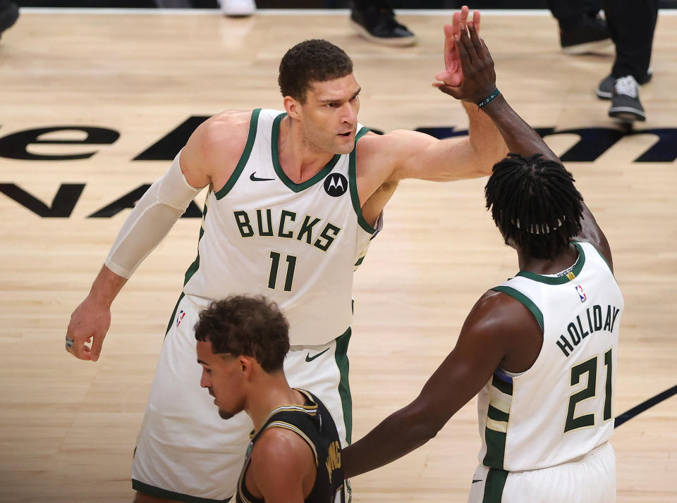 Trae Young #11 of the Atlanta Hawks hangs his head as Brook Lopez #11 and Jrue Holiday #21 of the Milwaukee Bucks celebrate a series win against the Atlanta Hawks in Game Six of the Eastern Conference Finals at State Farm Arena on July 03, 2021 in Atlanta, Georgia NOTE TO USER: User expressly acknowledges and agrees that, by downloading and or using this photograph, User is consenting to the terms and conditions of the Getty Images License Agreement. (Photo by Kevin C. Cox/Getty Images)