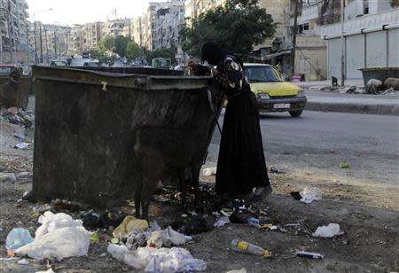 A woman searches for food in a rubbish container in the city of Aleppo in this July 31, 2013 file photo. REUTERS/ Loubna Mrie/Files