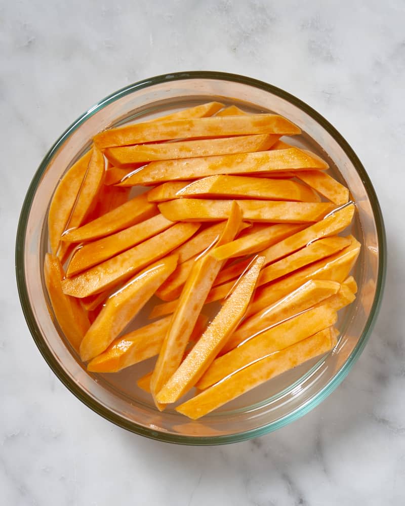 Overhead view of cut, raw,  sweet potato in a glass bowl covered by water.