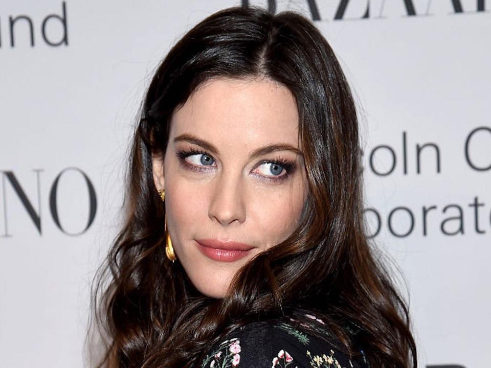 liv tyler wearing a black floral top in front of a white background