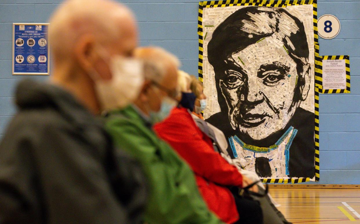 Patients sit in front of a portrait of Aneurin Bevan, the architect of the NHS, after receiving their booster vaccines in Cwmbran, Wales - Huw Fairclough/Getty Images Europe