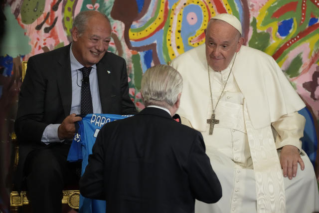Pope Francis, flanked by José María del Corral, president of Scholas Occurrentes, is presented by Napoli soccer club president Aurelio De Laurentiis with a Napoli jersey, during the world's first meeting of the 'Educational Eco-Cities' promoted by the 'Scholas Occurrentes', at the Vatican, Thursday, May 25, 2023. (AP Photo/Andrew Medichini)
