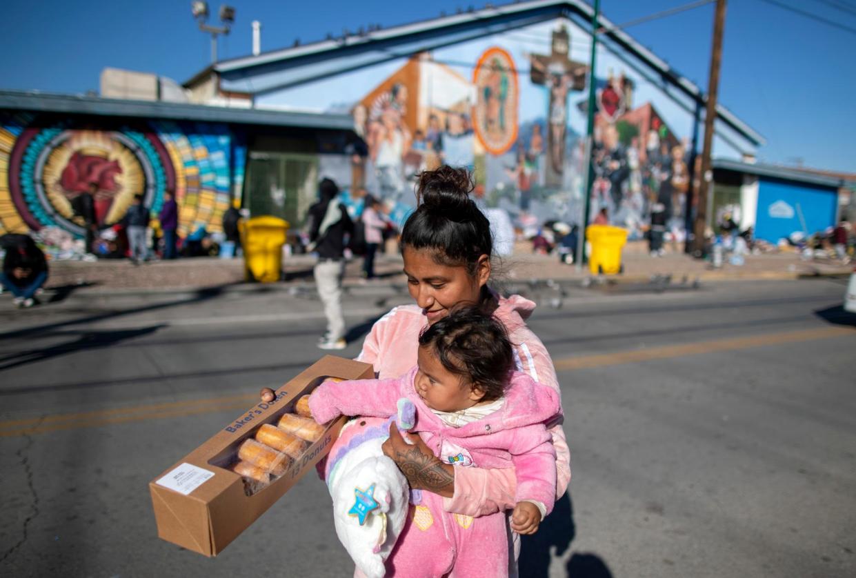 <span>A woman carries her baby and a box of donated donuts while camping outside the Sacred Heart shelter in El Paso, Texas, on 21 December 2022.</span><span>Photograph: Andres Leighton/AP</span>
