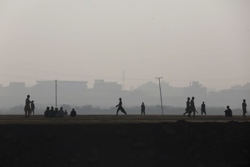 Children are silhouetted as they play cricket amid smog in Karachi