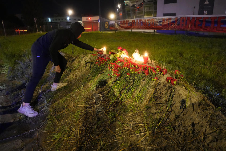 A man lights a candle at an informal memorial next to the former 'PMC Wagner Centre' in St. Petersburg, Russia, Thursday, Aug. 24, 2023, with a banner with words reading 'PMC Wagner, we are together' in the background. Russia's civil aviation agency says mercenary leader Yevgeny Prigozhin was on board a plane that crashed north of Moscow. (AP Photo/Dmitri Lovetsky)